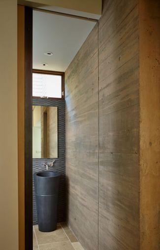 A concrete powder room wall plays off Stone Forest Veneto Sink and Mud Wood Chip Mosaic tile.