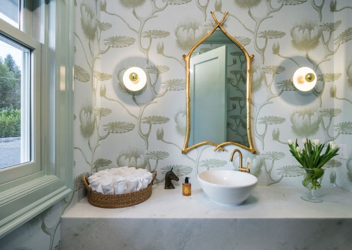 A powder room uses the same blue tones and brass accents as seen elsewhere but adds whimsy in the stylized lily wallpaper.