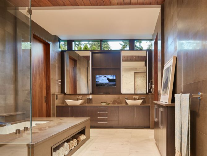 Designed to evoke a spa-like setting, the master bath boasts heated floors and tub deck, an extra-deep tub, and a hidden television set behind one of the vanity mirrors. The walls and tub surround are grey Fusano limestone, which has a lovely buttery texture. The cabinets are built from walnut.