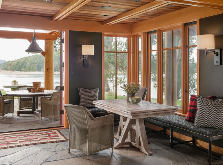 This cabin on the shores of San Juan Island invites the outdoors in at every turn. The same variegated blue stone used for the patio also forms the floor of the main entry room, creating a sense of continuity and cohesion. A built-in bench around two sides of the dining table keeps the small space streamlined, while the bank of windows in the corner provides an immediate connection to the shoreline just outside.