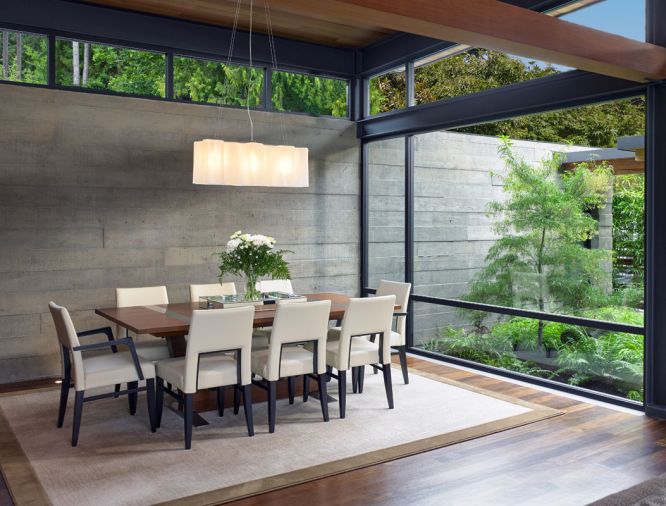 Board form concrete walls bring a warm industrial vibe to the dining room, while floor-to-ceiling windows introduce lush outdoor views. By designing the structure as well as the landscape, McClellan Architects ensures that everything works together.