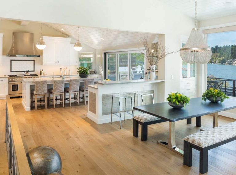 A reflective white lap siding ceiling brings light into kitchen. Phillip Jeffries grass cloth panels add panache to the bar. Curry & Co. French Empire crystal chandelier brings shine to Vanillawood sourced table; Kravet upholstered benches.