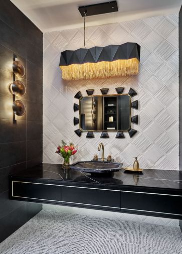A Mirror Image black leather and brass mirror sparkles amidst the black and white themed powder room. The sculptural light fixture by Arteriors softens the geometric elements found in the Kelly Wearstler flooring and tile wall by Ann Sacks.