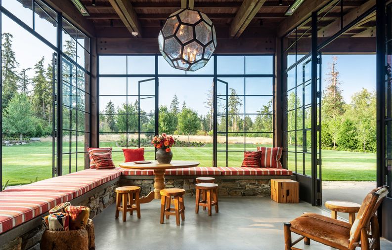 The sunroom is marked by a large, hexagonal-shaped hanging pendant custom designed by Kerry Joyce that is an unexpected contrast to the other, more rustic elements in the space. Steel-framed casement doors can open to let in fresh air, and an inglenook, or partially enclosed fireplace creates a sense of coziness. The sunroom’s meadow views are enhanced by pops of color in cushions with fabric from Romo and Great Outdoors, and fabricated by Washington company Island Custom Upholstery. Pendleton throw blankets and a classic table and stools by Tirto Furniture are a natural fit for the outdoorsy space, along with folding chairs from locally based Terris Draheim.