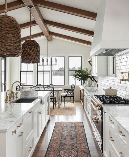 A modern palette of white, black, and gray pervades this farmhouse-style renovation, enhanced by brushed brass accents and fixtures in both the carriage and main house kitchens, which include cabinet design by Signature Design & Cabinetry. The water view is paramount from the kitchen and dining room, where a mix of the client’s own furniture and vintage pieces tie in with the marble countertops and wood accents. Windows by Sierra Pacific.