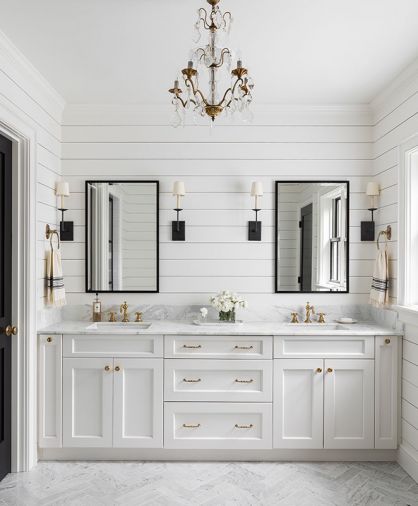 The master bathroom and powder room tie in multiple elements from the home, including marble countertops, black-framed mirrors and glass shower door that imitate the windows found elsewhere, shiplap walls, and brushed-brass hardware and fixtures. A cloudlike gray and white wallpaper in the powder room backs the client’s own vintage pine dresser repurposed into a vanity, with wall-mounted faucet and an antique mirror to round out the look.