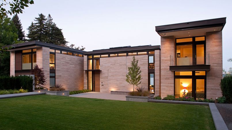 Amber Rose flame stone clad exterior is cut and stacked into three varied sizes to show texture and complex color range. Clerestory windows wrap the home for light yet ensure privacy from street. The Scot Eckley, Inc. landscape design features a gingko tree in a crushed gravel court at right; red Japanese maple left. Photo © Rob Perry
