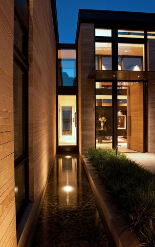 Two water features, running perpendicular to house, appear as if they carry water coursing through the house. Horizontal oak plank entry door echoes stacked stone façade. Large porcelain tile entry flooring is by Porcelanosa. Wndows are clad exterior/wood interior. Photo © Rob Perry