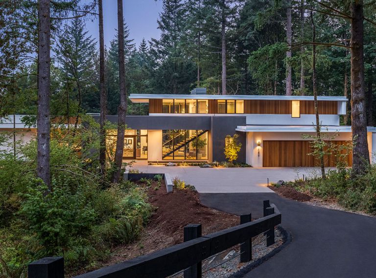 Sited on a 1.2 acre, heavily forested property, this home in the Portland area feels enveloped by the landscape. The exterior blends traditional stucco in two different shades as well as vertical red cedar. Wide overhangs protect the siding while also creating strong horizontal lines in contrast to the vertical cedar. A reflecting pool near the front entrance pulls in light and sets a spa-like tone even before you step inside.