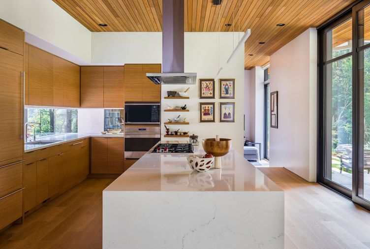 The kitchen ceiling using the same red cedar used for the exterior soffits creates a sense of continuity between indoors and outdoors. “We didn’t want to just have a lot of white surfaces, but we also didn’t want all wood surfaces, so this was a blend of bringing that warmth into the house without having it take over,” says Tim. The kitchen cabinetry and floors are white oak, while the wrap-around cabinetry in the entryway is walnut. The sleek kitchen is fitted with a Miele dishwasher, Miele oven, Wolf Cooktop, and a Sub-Zero refrigerator.