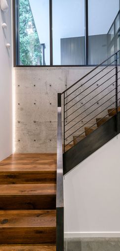 Walnut-stained oak staircase with steel railings travels from garage to Quantum entry door and black-stained sapele mahogany windows with aluminum cladding.