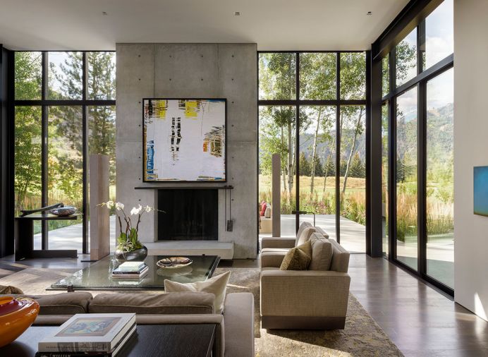 Barbara Vaughn photo of water on art lift reveals oversized TV on concrete fireplace with hot-rolled steel - wax finish mantel. Custom Gary Leeds audio speakers; William Morris glass art on custom Lucas Interior table. Lucas custom sofas; Driscoll Robbins rug.