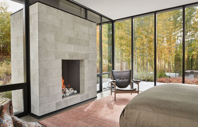 Finn Juhl Chieftain chair reproduction and artful kaleidoscopic mosaic tree trunk adjoin master hot-rolled steel fireplace. Lucas tweed coral/burgundy rug from Driscoll Robbins.