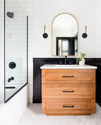 Delta Trinsic fixtures in Matte Black and School House Electric vanity sconces echo the black beadboard encircling guest bath, adding contrast against white porcelain tile floor and subway shower walls. Vanity countertop was installed by Venetian Stone Works.
