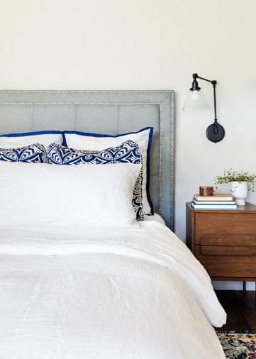 Serenity reigns in master bedroom: soft blue tufted headboard plays against geometric and blue trimmed pillows grounded by a floral bedside Joybird rug.