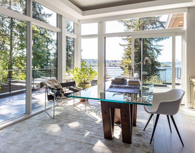 Moon captures forest and lake views from corner home office across wraparound terraces with custom steel railings, firepit, seating and staircase down to newly landscaped yard and reconfigured pool. Restoration Hardware 72' reclaimed V-form wood and glass dining table turned desk reminded homeowner of his alma mater “UW.” Ivory Hexa Hide rug and polished nickel Arc task floor lamp also by RH. Rug design repeats a “hive” theme found throughout the home. Soffit lighting when dimmed makes night-time view of lake sparkle.