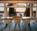 Sentient handcrafted live edge dining table from Brooklyn, New York, art studio glows beneath Cityscape Hubbardton Forge chandelier reiterating Seattle skyline beyond. Sierra Pacific accordion door.