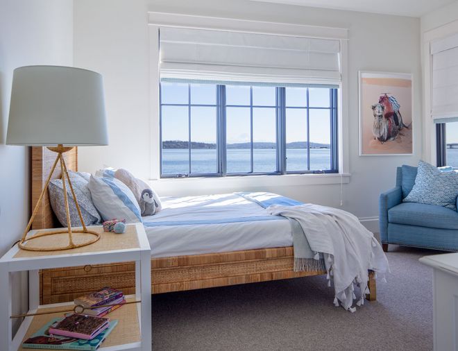 Black-framed Sierra Pacific windows (used throughout) capture the water views, and a chair upholstered in blue fabric cozies a corner. The woven bed frame by Serena & Lily adds textural interest.