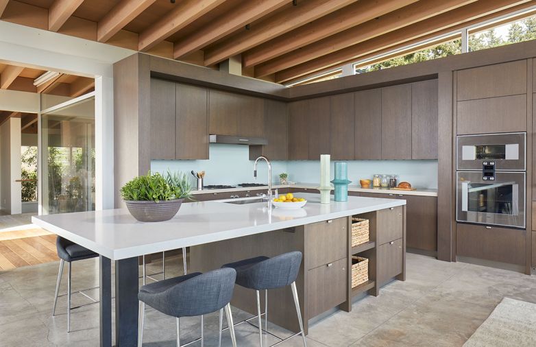 In the kitchen, Gaggenau appliances, including the wall oven, cooktop, and hood vent, as well as the Miele dishwasher and Sharp microwave (not pictured), are all from Albert Lee Appliance. The open floor plan allows for full view of the living room, outdoor pools and Lake Washington.