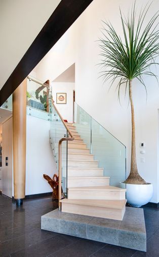 A two-story-tall cedar and steel column flanks the glass-enclosed staircase, the expansive soft white walls leave space for the homeowners to continue growing their art collection.
