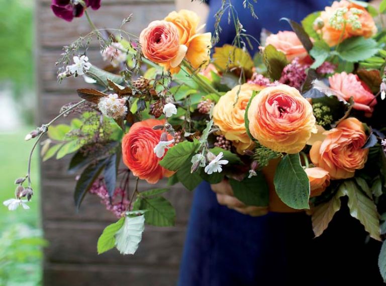 Eye-catching orange and chocolate tones highlight a bouquet of copper beech, black elderberry, ranunculus, sweet peas, grasses, mallow, nine bark, bronze fennel and snowberry foliage.