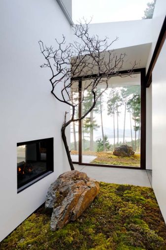 Budget-friendly, green building solutions include a double-sided steel manufactured fireplace found on Craigslist and framed in black-painted glass that reflects the outdoors. Live moss, rock and a dried Madrona branch greet guests, maintaining visual flow of natural vegetation from outdoors in.