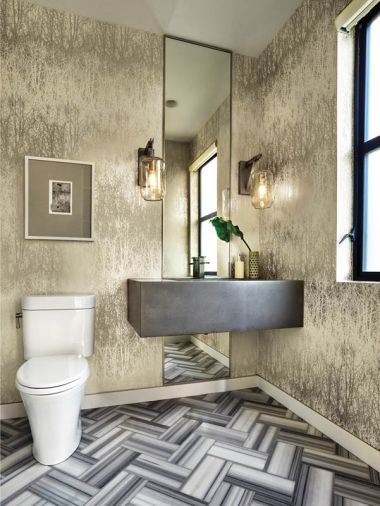 Inspiration for the downstairs powder bath began with the crisp lines of Bianco Striata marble floors in a chevron pattern. The silvery Birches wallpaper is by Schumacher. A floor to ceiling mirror rises behind the cement sink crowned by LBL Lighting sconces.