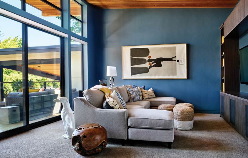 The vertical cedar ceiling in the upstairs family room at right is carried out into the wing-like architecture overhanging the large concrete porch - suitable, says the woman, for hanging out and watching the stars. Rich blue walls and painted baseboards create a warm, enveloping space for cozy family fun. Katyama artwork ties indoors with outside.
