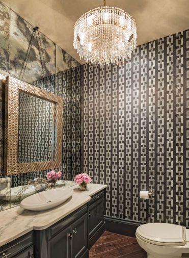 In the guest powder room, the application of tones was reversed from that seen in the living and dining areas with the use of a darker wallpaper and dark cabinetry. Yet Baines maintained a feeling of airiness by hanging a mirror on a wall of mirrors and installing a new counter top.