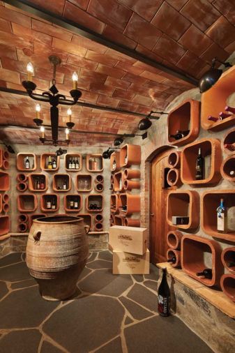 Chimney flue tiles double as wine bottle storage, adding a whimsical touch to the fan shaped wine cellar.  “Edifice Construction did a great job with a challenging space,” says Gelotte, who used piles of mortar to keep the flue tiles in place. A traditional arched ceiling with terra cotta tile and steel beams is topped with concrete.