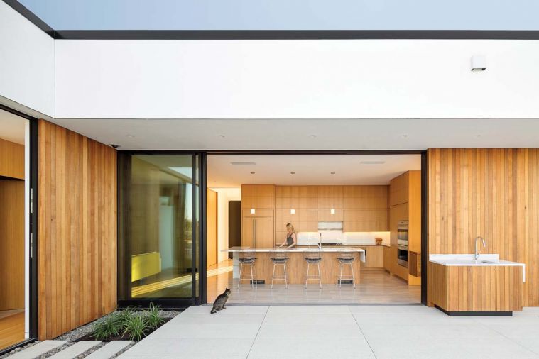 Ash+Ash beautifully achieves one of the core tenants of modern architecture: blurring the boundaries between indoors and outdoors. A paneled sliding glass door allows the wall between the kitchen and pool terrace to be eliminated completely. Exterior cedar cladding in similar tones to the kitchen cabinetry, as well as shared design elements between the main kitchen and outdoor sink and countertop, provide visual links between the interior and exterior of the home. The terrace is paved in locally fabricated, pre-stressed concrete pavers, which are smooth and durable as well as low-emissivity.