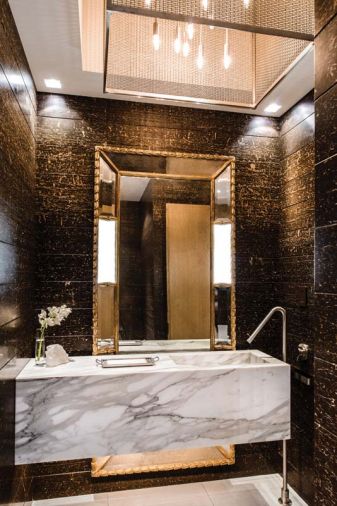 Custom carrara marble vanity and natural stone walls, gilded mirror and chandelier by GCW distinguish the first of two powder rooms