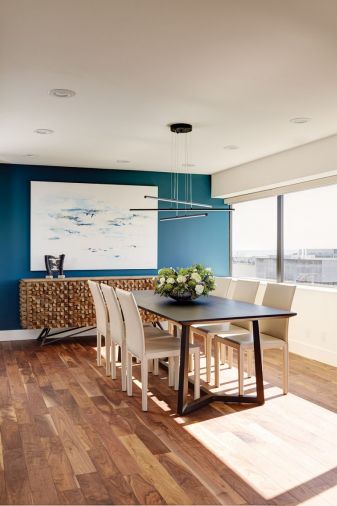 In the kitchen and dining room, chartreuse chairs contrast brightly against a cool-toned dark oak cabinetry. To the left, a red and teal painting by Dale Chihuly provided initial design inspiration, and brings an active, joyful energy to the space. To the right, another white and blue canvas from Mya Kerner echoes the teal color of the accent wall, while a natural wood sideboard from Anthropologie adds dynamic, almost hedgehog-like texture.