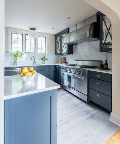 The combination of navy cabinetry with white countertops and tile gives a crisp, tailored look. Because the family cooks frequently, Heather opted for a durable quartz product for the countertops and oven backsplash, finished to resemble Calcutta marble.