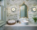 A powder room uses the same blue tones and brass accents as seen elsewhere but adds whimsy in the stylized lily wallpaper.