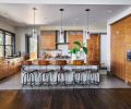 Slip matched walnut veneer cabinets frame the kitchen, while a sliding barn door keeps any disarray in the working pantry from view. Quasi industrial pendants trimmed in black hail back to the windows. A dropped kitchen ceiling helps regulate the busy sounds of kitchen prep and chatter. At right is the passageway to the mudroom, laundry/crafts room, pool bath, and staircase to the upstairs family rec room, gym and secondary bath. Door to the patio is at left.