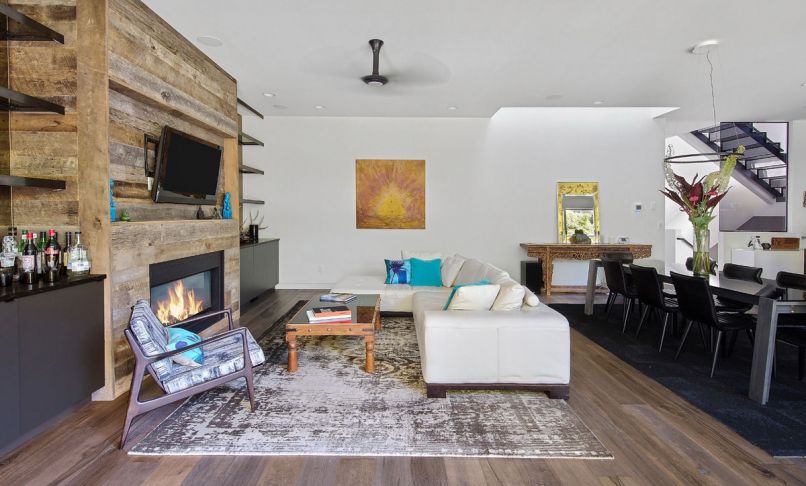 Natural materials soften the contemporary look of the living area: reclaimed wood, an antique style wool rug, leather couch and a 15th-century Ming Dynasty wood table. Tinted mirrors behind the shelving add depth and warmth.