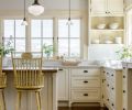 The traditional farmhouse kitchen is built around custom cabinetry from Warmington & North, a Seattle-based cabinetry specialist. Warm neutral tones on the walls, cabinets, area rug, and furniture enhance the glow that comes from wrap-around windows.