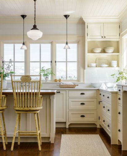 The traditional farmhouse kitchen is built around custom cabinetry from Warmington & North, a Seattle-based cabinetry specialist. Warm neutral tones on the walls, cabinets, area rug, and furniture enhance the glow that comes from wrap-around windows.