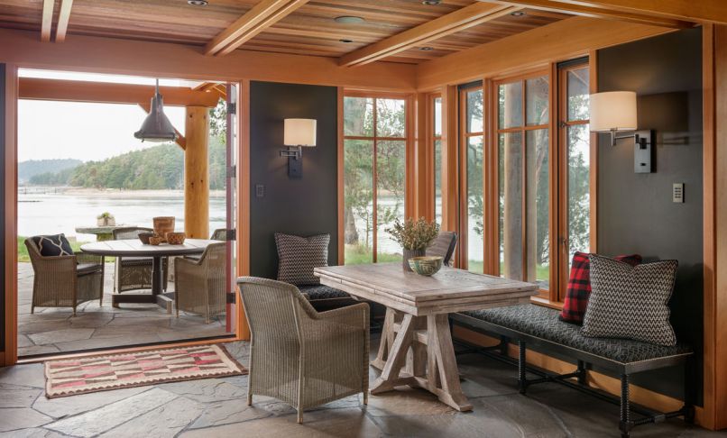 This cabin on the shores of San Juan Island invites the outdoors in at every turn. The same variegated blue stone used for the patio also forms the floor of the main entry room, creating a sense of continuity and cohesion. A built-in bench around two sides of the dining table keeps the small space streamlined, while the bank of windows in the corner provides an immediate connection to the shoreline just outside.