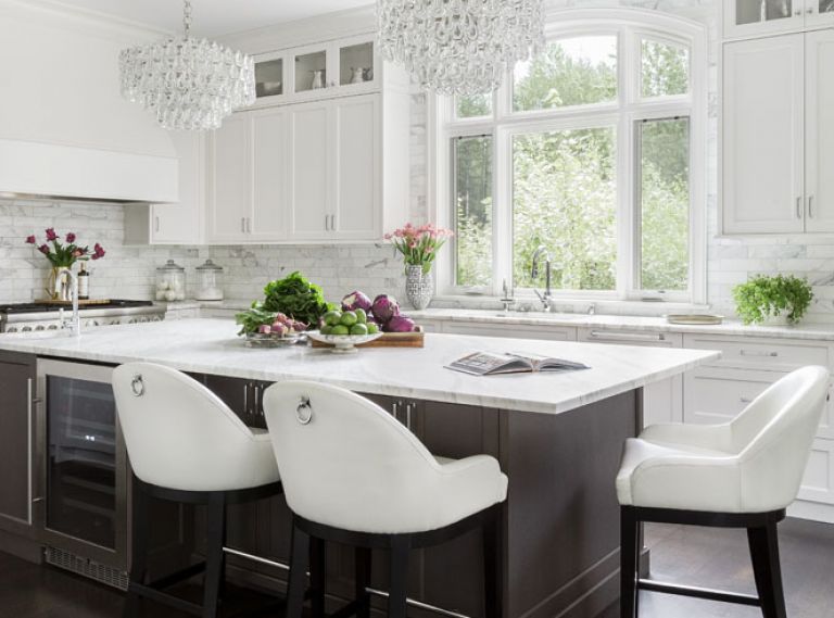 Custom cabinetry from Northwest Custom Cabinets stretches all the way to the ceiling, eliminating awkward unused spaces at the top. Jewelry-like chandeliers add feminine sparkle to the room, while warm-toned dark hardwood floors create an anchoring base for all those bright surfaces. The Thermador range and oven includes a main oven and a steam oven, making it ideal for entertaining family or clients.