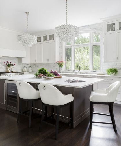 Custom cabinetry from Northwest Custom Cabinets stretches all the way to the ceiling, eliminating awkward unused spaces at the top. Jewelry-like chandeliers add feminine sparkle to the room, while warm-toned dark hardwood floors create an anchoring base for all those bright surfaces. The Thermador range and oven includes a main oven and a steam oven, making it ideal for entertaining family or clients.