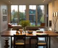 A crisp, clean-lined fireplace with a cantilevered honed quartz slab hearth anchors an open dining and living room layout. As the sun moves across the sky, shadows from the grid windows play across the fireplace wall.