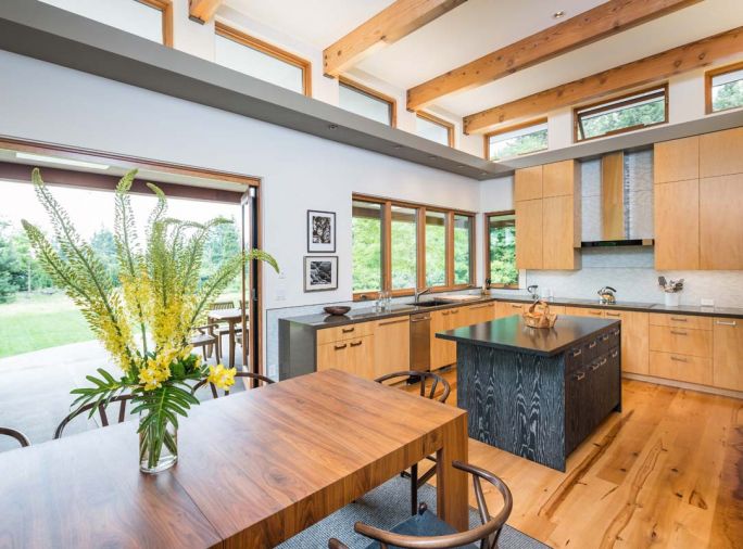 In the kitchen, a motorized control allows residents to open the clerestory window above the range for natural ventilation. White ceilings with exposed wood beams give it a crisp, farmhouse-inspired look. “We wanted the ceilings to be as light as possible so the interior would glow with natural light,” says architect Nathan Good.