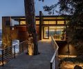 A simple-span bridge accommodates a towering fir, which mimics the monolithic column at left that houses the outdoor kitchen with deck.