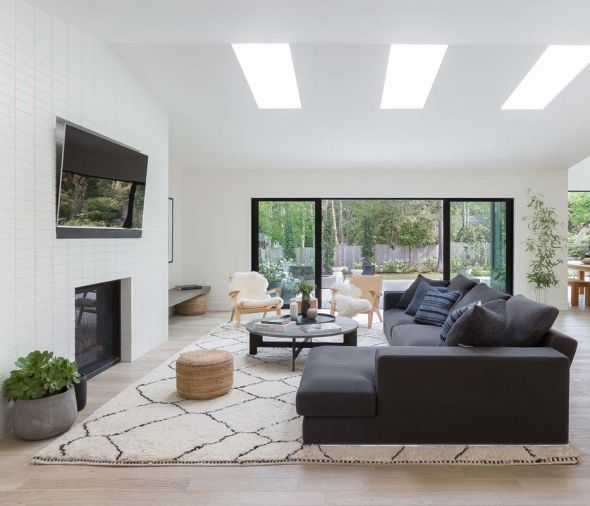 Generous Pella sliding glass doors and wood floors help pull the forested backyard and living room together. Sectional by Camerich, coffee table by Four Hands, and Jute Ottomans by Safavie add modern flair.