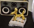 Jeff Koons gold balloon dog prances before Ezra Cimino-Hurt black and white Case of Bass boombox.