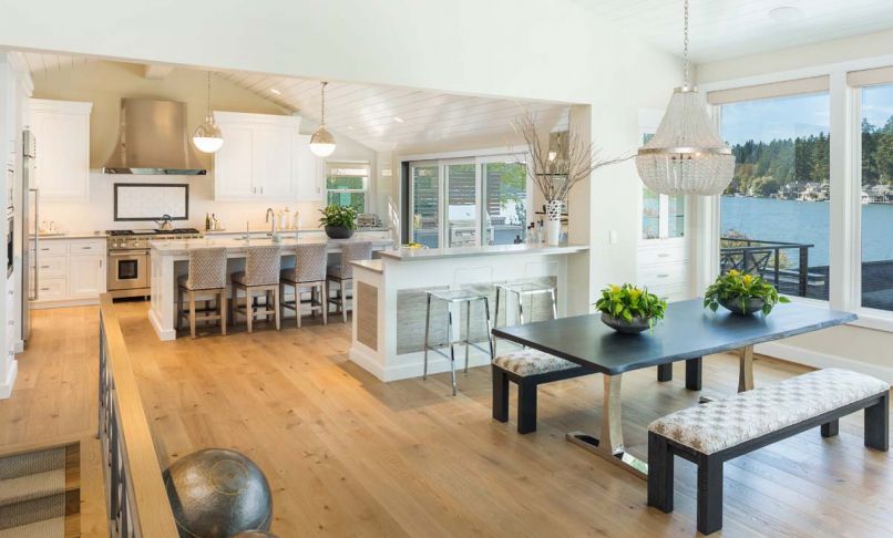 A reflective white lap siding ceiling brings light into kitchen. Phillip Jeffries grass cloth panels add panache to the bar. Curry & Co. French Empire crystal chandelier brings shine to Vanillawood sourced table; Kravet upholstered benches.