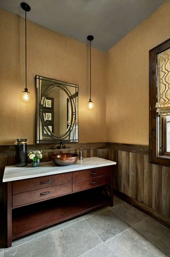 The powder bath features a pair of Baltimore Classic Cord pendants from Rejuvenation. Wainscoting fashioned from the same rustic Provenza flooring found throughout the home contrasts with tile flooring. By contrast, the wine room is lit by an Industrial Cage Filament Pendant by Restoration Hardware above a warm stone tile floor.