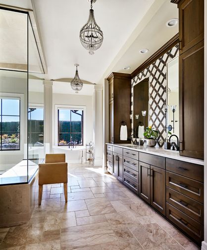 The master suite is elegance personified, with a heated Versailles patterned marble floor in the bath and artful pairing of marble and wood backsplash. Chandeliers and a bathtub in an alcove. Cabinetry throughout the home by Hayes Cabinets.